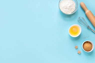 Mutfak aletleri ve malzemeler. Yumurta, un, şeker, çırpma ve mavi arka planda merdane. Pişirme konsepti düz yatay, kopyalama alanı.