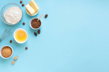 Mutfak aletleri ve malzemeler. Yumurta, un, kakao fasulyesi ve pudra, şeker, çırpı ve mavi arka planda merdane. Pişirme konsepti düz yatay, kopyalama alanı.