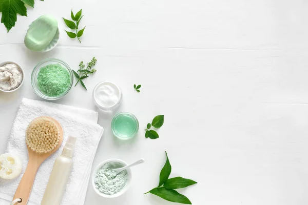 Natural eco beauty treatment. Cosmetic products, towel and green leaves on white background, top view, copy space. Natural organic skincare, spa, healthy lifestyle concept.