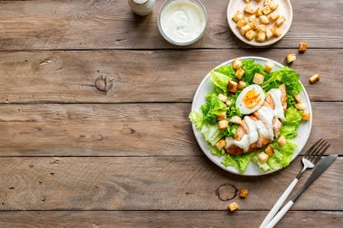 Tahta arka planda tavuk göğsü olan Sezar salatası, üst manzara, fotokopi alanı. Sağlıklı öğle yemeği için taze tavuk salatası..