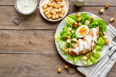 Tahta arka planda tavuk göğsü olan Sezar salatası, üst manzara, fotokopi alanı. Sağlıklı öğle yemeği için taze tavuk salatası..