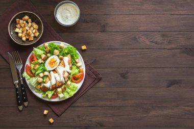 Koyu ahşap arka planda tavuk göğsü olan Sezar salatası, üst manzara, kopyalama alanı. Sağlıklı öğle yemeği için taze tavuk salatası..