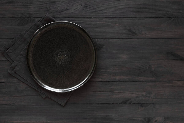 Пустой круглый черный номер на темном черном фоне, вид сверху, пространство для копирования. Керамическое черное блюдо на деревянном столе, макет
.