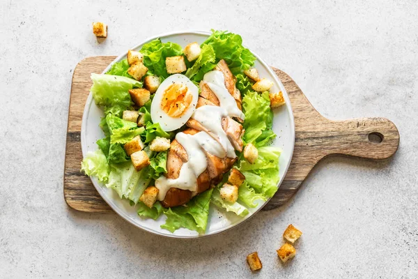 Caesar salad with chicken breast on white background, top view, copy space. Fresh chicken salad for healthy lunch.