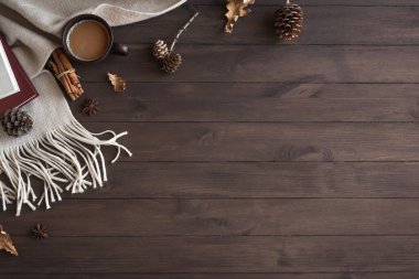 Yumuşak ekose ve bir fincan kahveyle rahat bir kompozisyon. Mevsimlik sonbahar ya da kış sıcacık battaniye, kahve, kitap ve çam kozalakları. Konforlu ev ve ahşap zemin üzerindeki hygge konsepti, kopyalama alanı.