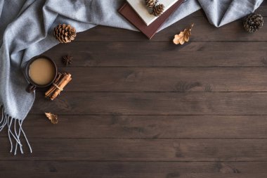 Gri yumuşak ekose kumaş ve bir fincan kahveyle sonbahar kompozisyonu. Sıcak battaniye, kahve, kitap, yaprak ve koni ile mevsimsel sonbahar konforu. Konforlu ev ve ahşap zemin üzerindeki hygge konsepti, kopyalama alanı.