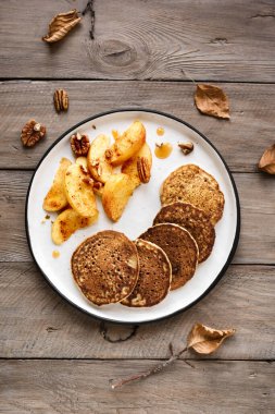 Sonbahar kahvaltısı. Karamelli elmalı krepler, fındıklı fındıklar ve ballı ahşap masa, üst manzara. Sağlıklı mevsimlik vejetaryen yemeği.