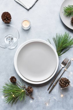 Noel Masası Ayarlama, çam dallı boş tabak, koniler, açık gri masadaki mumlar, üst manzara, kopyalama alanı. Noel yemeği, parti tasarımı, konsept.