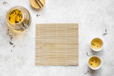 Çay konsepti - şeffaf çaydanlık ve yeşil çay fincanları ve bambu paspası. Beyaz arkaplanda geleneksel yeşil çay kompozisyonu, kopyalama alanı, üst görünüm.