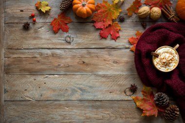 Sonbahar kompozisyonu - Balkabağı Baharatlı Latte, ılık eşarp, sonbahar akçaağaç yaprakları ve balkabağı ahşap arka planda, yaratıcı düzlük, üst manzara, kopyalama alanı. Kahve içilen mevsimlik sonbahar konsepti.