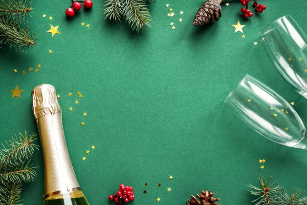 Christmas composition. Champagne, Christmas decor, pine branches and golden confetti on green background. Festive flat lay, top view, copy space.