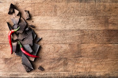Kara Çikolata Arkaplanı. Parçalanmış çikolata parçaları, ahşap masa üzerinde kırmızı biber, üst görünüm, boşluk kopyala.