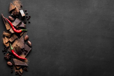 Kara Çikolata Arkaplanı. Çikolata parçaları, kakao tozu, acı biber ve baharatlar siyah masada, üst manzara, kopyalama alanı.