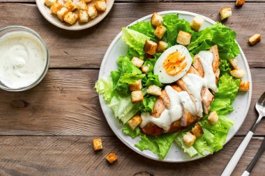 Tahta arka planda tavuk göğsü olan Sezar salatası, üst manzara, fotokopi alanı. Sağlıklı öğle yemeği için taze tavuk salatası..