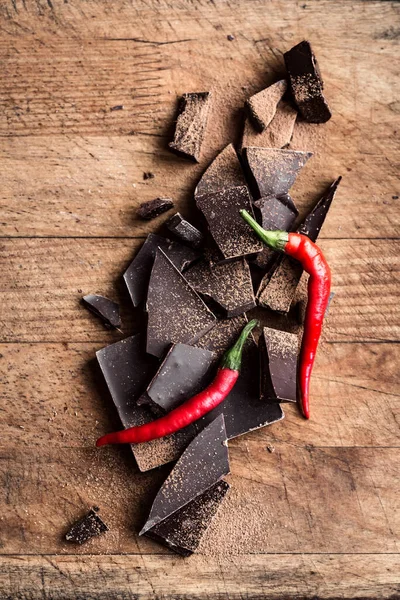 Kara Çikolata Arkaplanı. Parçalanmış çikolata parçaları, ahşap masa üzerinde kırmızı biber, üst görünüm, boşluk kopyala.