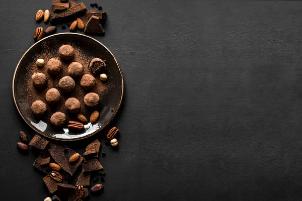 Chocolate truffles with dark chocolate and nuts on black background, top view, copy space. Vegan homemade chocolate energy balls or truffles for dessert.