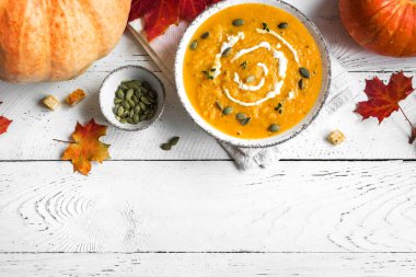 Balkabağı çorbası ve beyaz ahşap masa üzerinde organik balkabakları, üst görünüm, kopyalama alanı. Mevsimlik sonbahar yemekleri - Baharatlı balkabağı ve havuç çorbası.