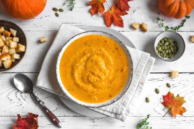 Balkabağı çorbası ve beyaz ahşap masa üzerinde organik balkabakları, üst görünüm, kopyalama alanı. Mevsimlik sonbahar yemekleri - Baharatlı balkabağı ve havuç çorbası.