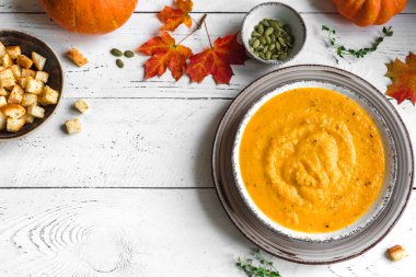 Balkabağı çorbası ve beyaz ahşap masa üzerinde organik balkabakları, üst görünüm, kopyalama alanı. Mevsimlik sonbahar yemekleri - Baharatlı balkabağı ve havuç çorbası.