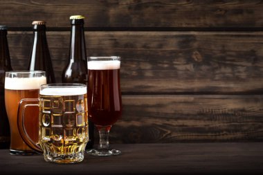 Şişelerde çeşitli bira fıçıları, bardaklar ve kupalar ahşap masa üzerinde, fotokopi alanı. Taze bira..