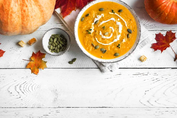 Balkabağı çorbası ve beyaz ahşap masa üzerinde organik balkabakları, üst görünüm, kopyalama alanı. Mevsimlik sonbahar yemekleri - Baharatlı balkabağı ve havuç çorbası.