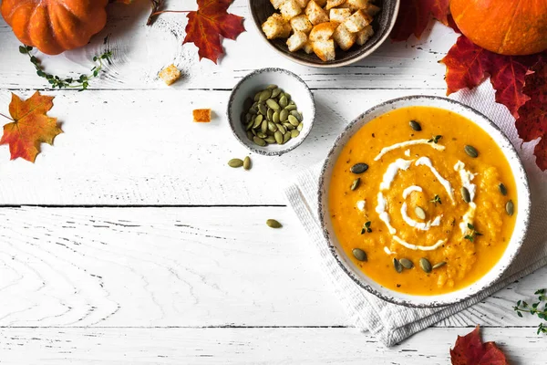 Balkabağı çorbası ve beyaz ahşap masa üzerinde organik balkabakları, üst görünüm, kopyalama alanı. Mevsimlik sonbahar yemekleri - Baharatlı balkabağı ve havuç çorbası.