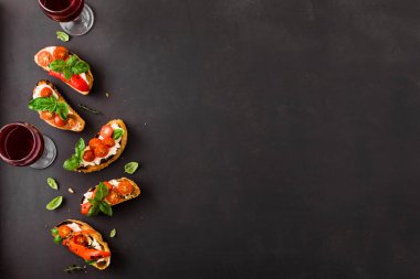 Domatesli, krem peynirli, kırmızı biberli ve fesleğenli sandviçler koyu arka planda, üst manzara, fotokopi alanı. Şarap için geleneksel İtalyan aperatifi. Izgara bruschetta tostu..