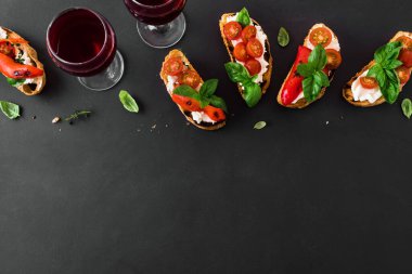 Domatesli, krem peynirli, kırmızı biberli ve fesleğenli sandviçler koyu arka planda, üst manzara, fotokopi alanı. Şarap için geleneksel İtalyan aperatifi. Izgara bruschetta tostu..