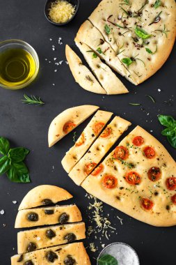 İtalyan Focaccia Ekmeği. Siyah arka planda çeşitli dolgular var. Domatesli, zeytinli, sarımsaklı ve otlu taze pişmiş Focaccia..