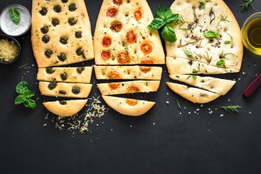 İtalyan Focaccia Ekmeği. Siyah arka planda çeşitli dolgular var. Domatesli, zeytinli, sarımsaklı ve otlu taze pişirilmiş Focaccia, üst görünüm, kopyalama alanı.