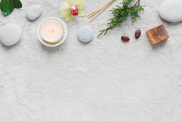 Natural Skin Care and Spa Set on white soft towel background with natural cosmetic products, flower, green leaves, candle and zen like stones. Relax concept, top view, copy space.