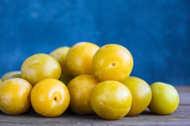 Ahşap rustik arka plan ve Mavi Kadife duvar emaye Kupası'nda taze Sarı Erik. Rus ev yapımı meyve. Önden görünüm. Kopya alanı