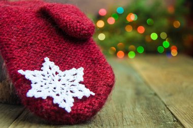Kırmızı yün mitten rustik ahşap arka plan üzerinde beyaz pamuklu tığ işi kar tanesi ile. Noel ışıkları kırmızı, mavi, sarı ve yeşil noktalar. kürk ağaçta. Kart, kart kavramı. Önden görünüm. Bokeh.