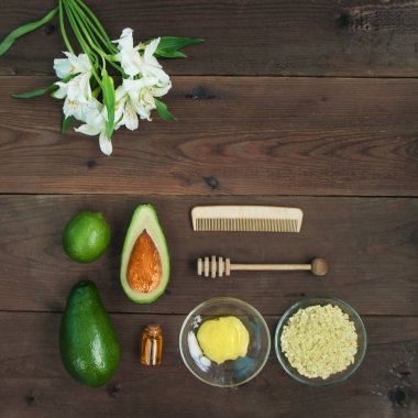 Malzemeler vitamini Avokado cilt bakımı cilt bakımı için maske yeşil limon, şişe Kozmetik yağı, bal, kepçe, yulaf gevreği, kahverengi ahşap zemin üzerinde saç fırçası. Alstroemeria çiçek. Üstten görünüm Kopyala yer kapatın