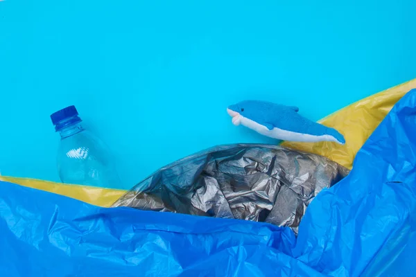 Blue dolphin swims in yellow, black plastic waste and trash floating in the ocean with copy space. Pollution concept. Toop view, flat lay