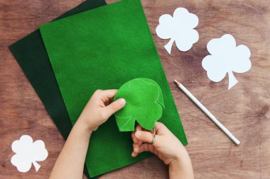 Çocuk elleri bir kağıt desen yonca üzerinde makas ile keçe yün kesilmiş, trefoil, ahşap arka plan üzerinde beyaz kalem ile İrlanda St Patrick günü için yeşil yaprakları ile shamrock. Diy kavramı. Üstte görüntü