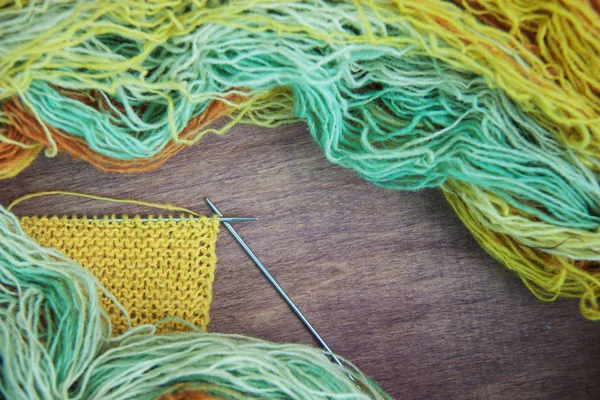 Knitting of yellow and blue wool with needles on wooden rustic background. Copy space, top view, flat lay