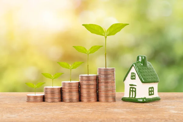 Model house and coin stack with tree on blur green background mortgage saving concept