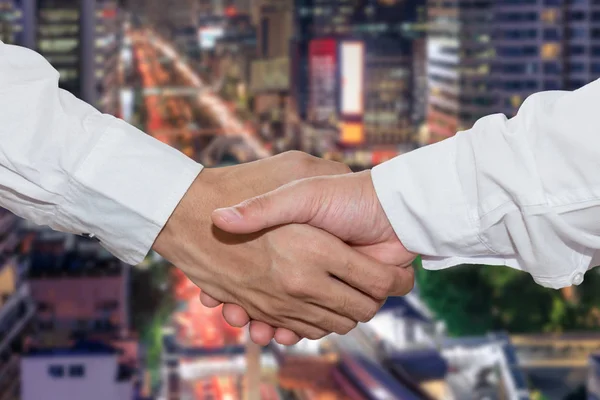 Business people shake hand in front of financial district at night