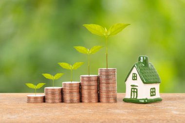 Model ev ve bozuk para yığını bulanık yeşil arka planda ağaç.