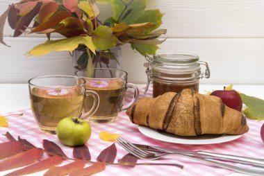Çay bir kruvasan ile peçeteye iki bardak. Sonbahar yaprakları ve elma masaya vardır