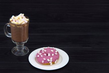 Bir cam fincan kakao marshmallows ile pembe krema ve Marshmallow siyah bir ahşap zemin üzerine beyaz bir tabakta donut