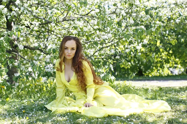 girl in a yellow spring dress against the background of a blossoming apple tree