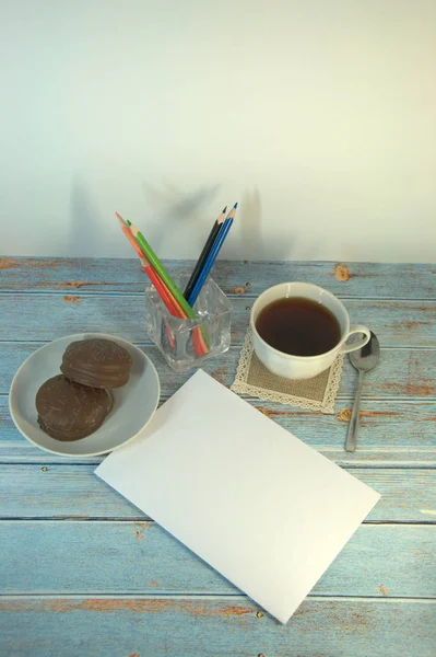 A cup of tea, spoon, teralka with chocolate cookies and pencils on a wooden table. Close-up.