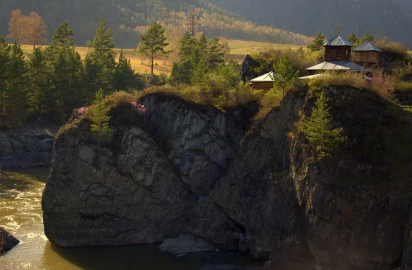 An Orthodox chapel on the edges of a high cliff and a swift mountain river flowing at the foot. Altai, Siberia, Russia.