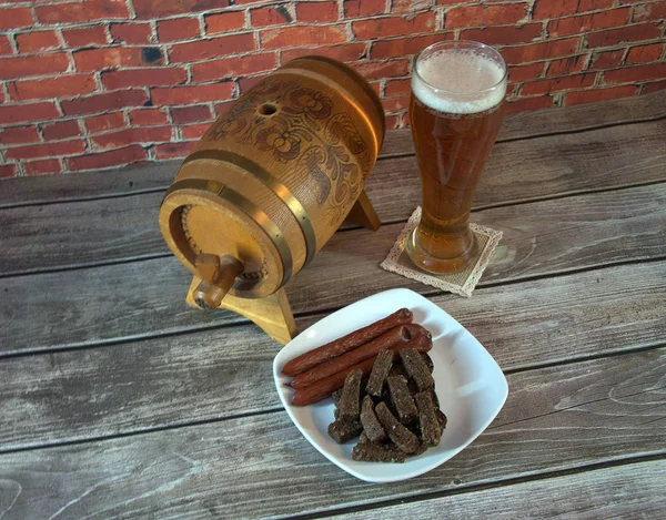 Wooden keg, glass of light beer and a plate with snacks on the table. Close-up.