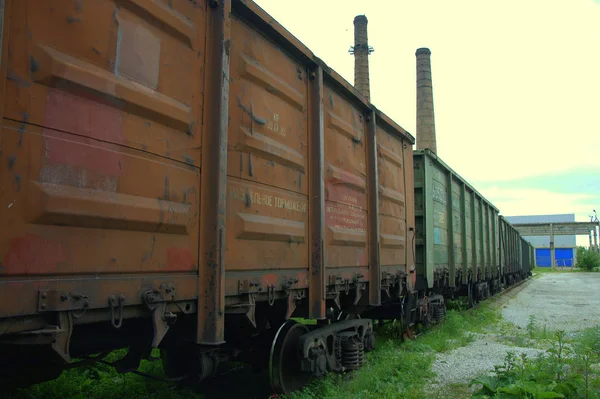 Railway cars are at an impasse in front of the old plant on the background of pipes. Industrial landscape.