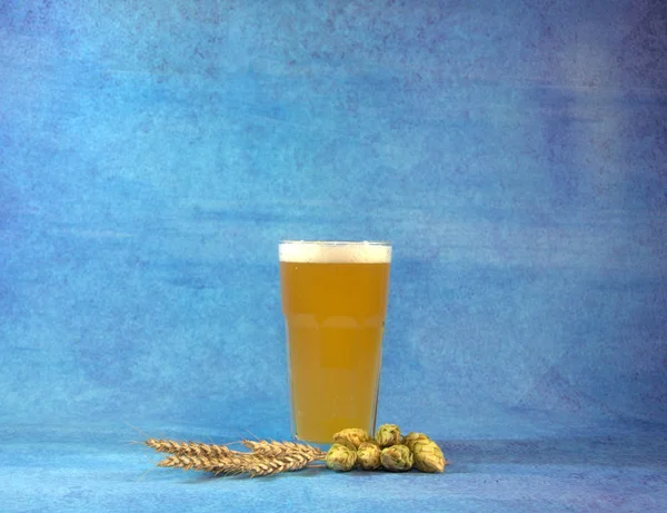 Glass of wheat beer with hops and sprinkles on a blue abstract background.