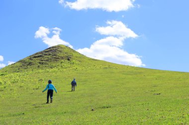 Aktif yaşam tarzı, turizm, yürüyüş ve konsept. Güneşli bir öğleden sonra. Dağlardaki muhteşem manzara. Çimenli yuvarlanan tepe. Mavi gökyüzü ve bulutların üzerinde yeşil tepede koşan iki genç çocuk..