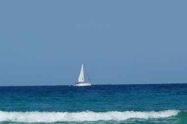 White sailing boat on the horizon of blue sea matches to foam of wave in Scala Potamia Thassos. Summer 2018 clipart